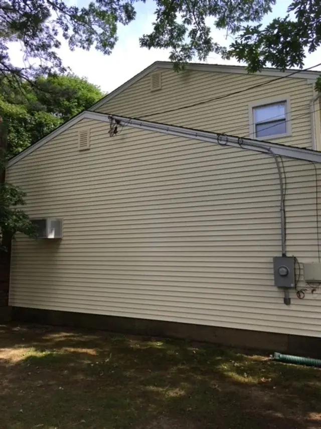 Clean beige vinyl siding on the side of a house under trees