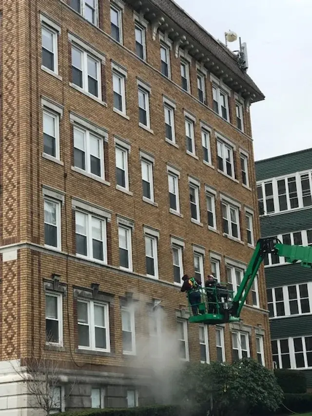 Tan brick apartment building with a green boom lift and wash spray at the lower floors