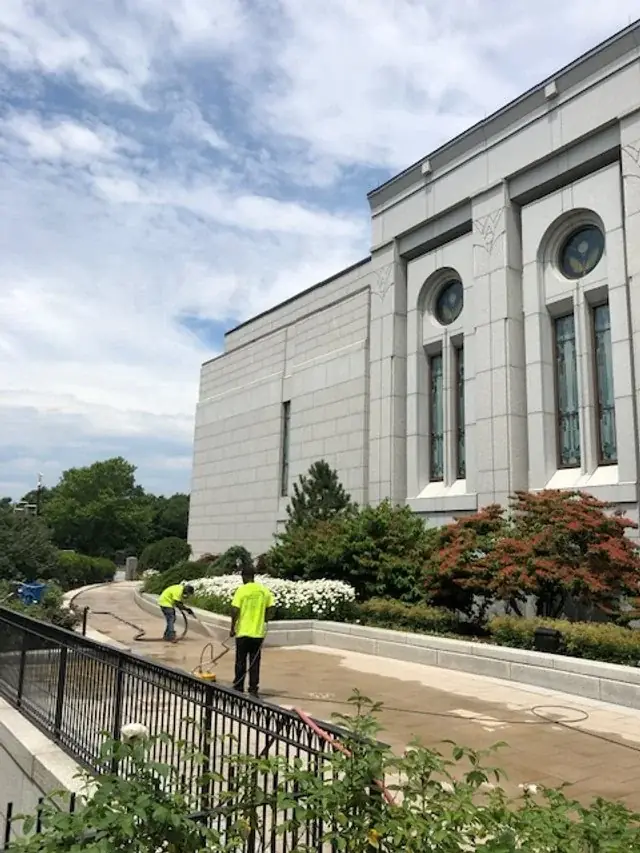 Pale limestone building exterior with arched windows and a crew washing the plaza