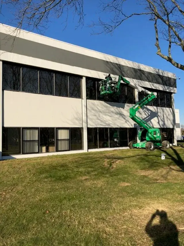 Green boom lift raised against the ribbon windows of a two-storey commercial building