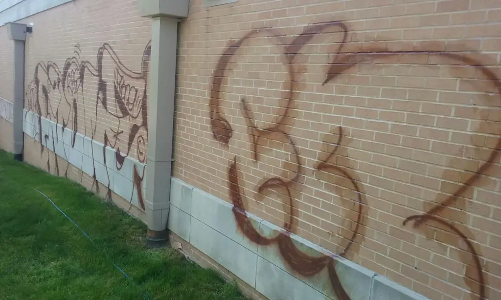 Red-brown spray-paint tags across a tan brick wall above a pale stone base course