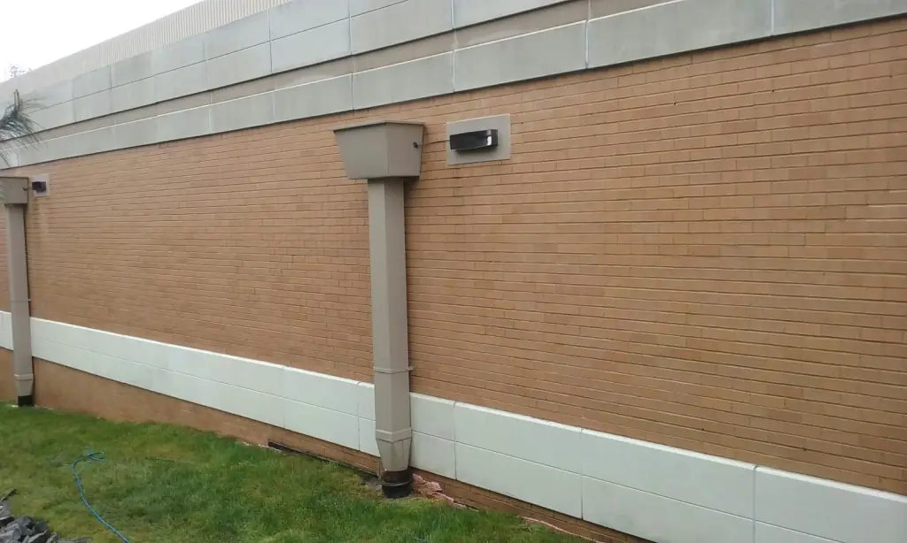 The same tan brick wall with the spray paint gone and the pale stone base course clean